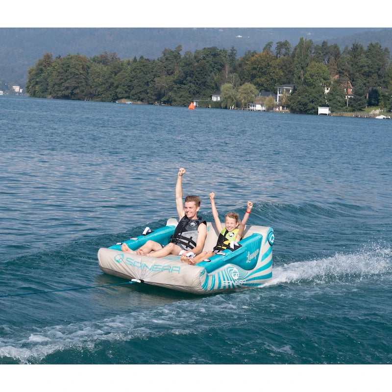 Two people enjoying a ride on a boating tube in the water with a scenic background