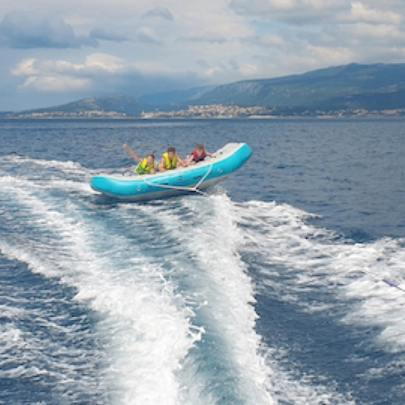 Three people on an aqua inflatable boat tube in the ocean with mountains in the background