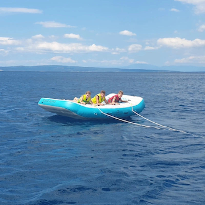 Three people on a small blue and white boat tube in the middle of a large body of water with clear skies