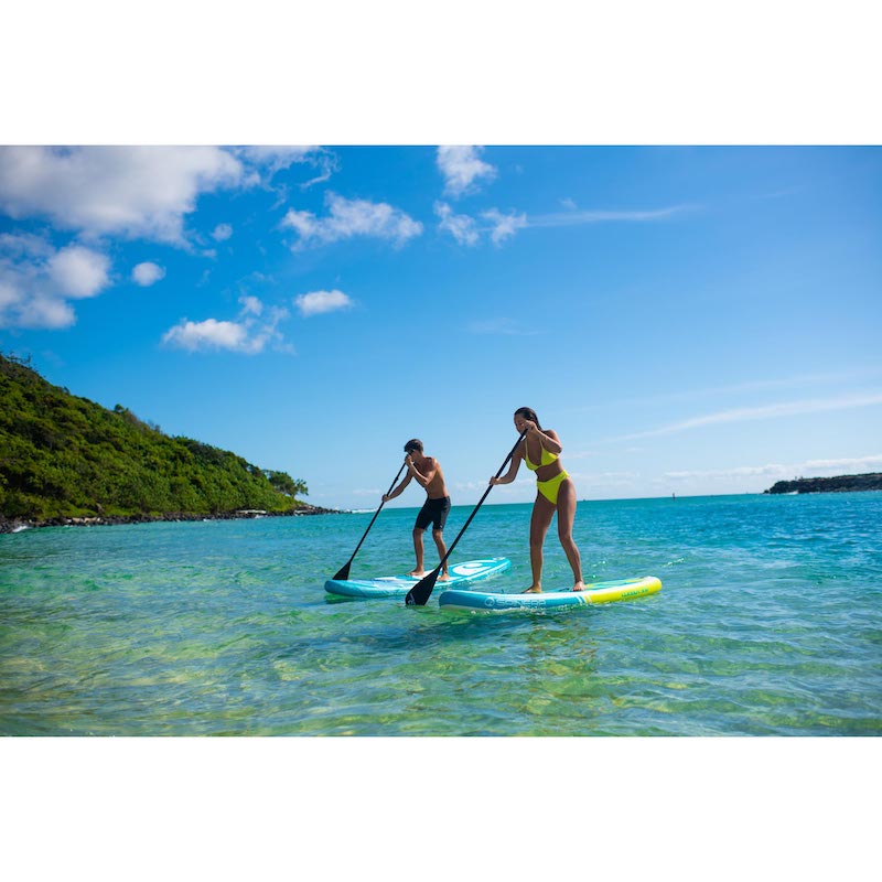 Two people paddleboarding on a clear blue sea with a scenic background