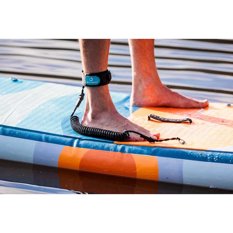 Person standing on a paddleboard with a leash around their ankle, on a body of water.