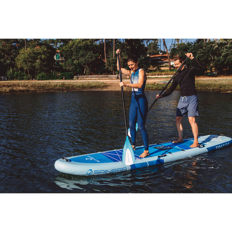 Two people on a stand-up paddleboard in a body of water with trees in the background.