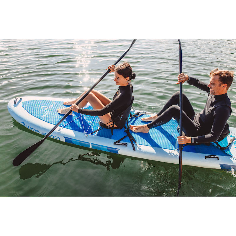 Two people paddleboarding on a blue and white board in calm water.