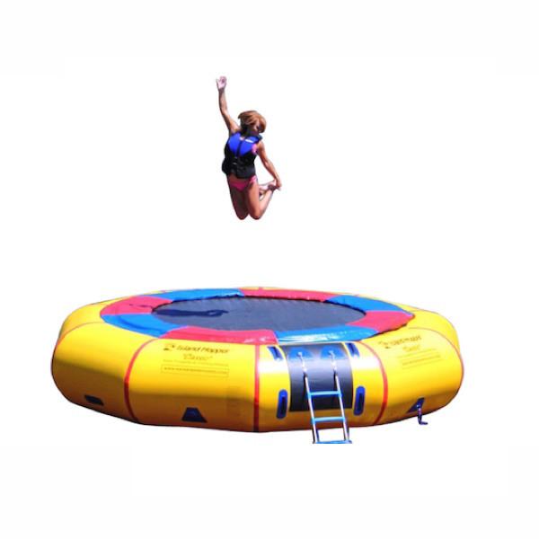 Girl jumping on the Island Hopper 15&#39; Classic Water Trampoline on a white background.  Yellow inner tube, black trampoline surface, red and blue trim. 