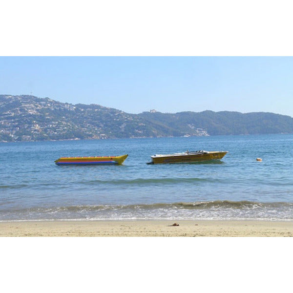 Boat pulling an unoccupied Island Hopper 8 Person Towable Banana Boat Tube near the beach on the ocean at no wake speed. 