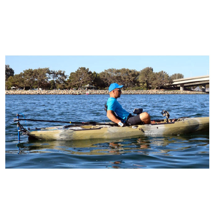 Bixpy Pole Steering system attached to a kayak and in use out on the water. Steered by a man in blue hat and t shirt and lack shorts. The kayak is pea green with white and grey to blend as camouflage. 