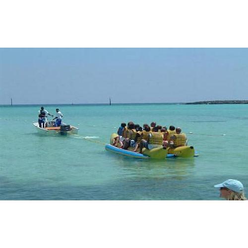 Island Hopper 10 Man Banana Boat Tube full of passengers beginning to be pulled out from shore on clear, green blue ocean away from shore. 