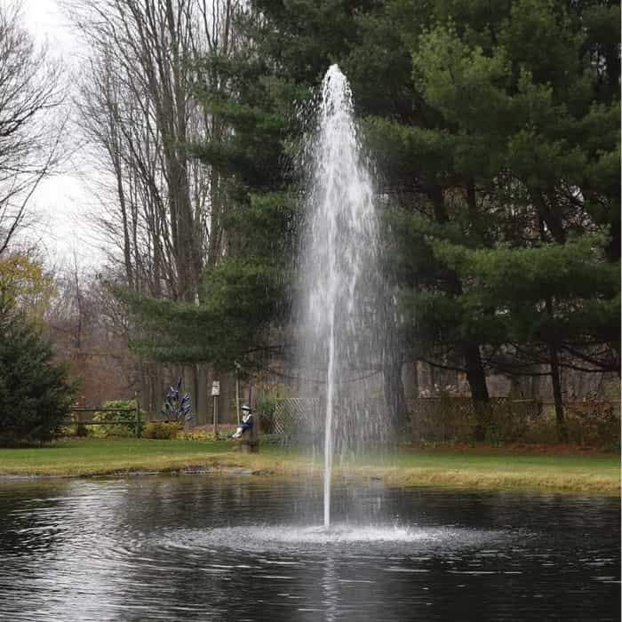 Easy Pro ACF1 Floating Fountain Head with Rocket Nozzle spraying up a single stream in the middle of a small pond.  The small pond fountain head sprays almost 25ft high.  Green grass and then trees surround the visible edge of the small pond.