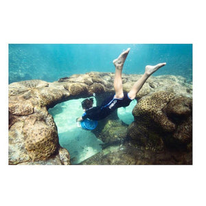 A teenager using a Yamaha Explorer Seascooter while scuba diving through an opening in a reef.  The water is well lit and the picture is bright.
