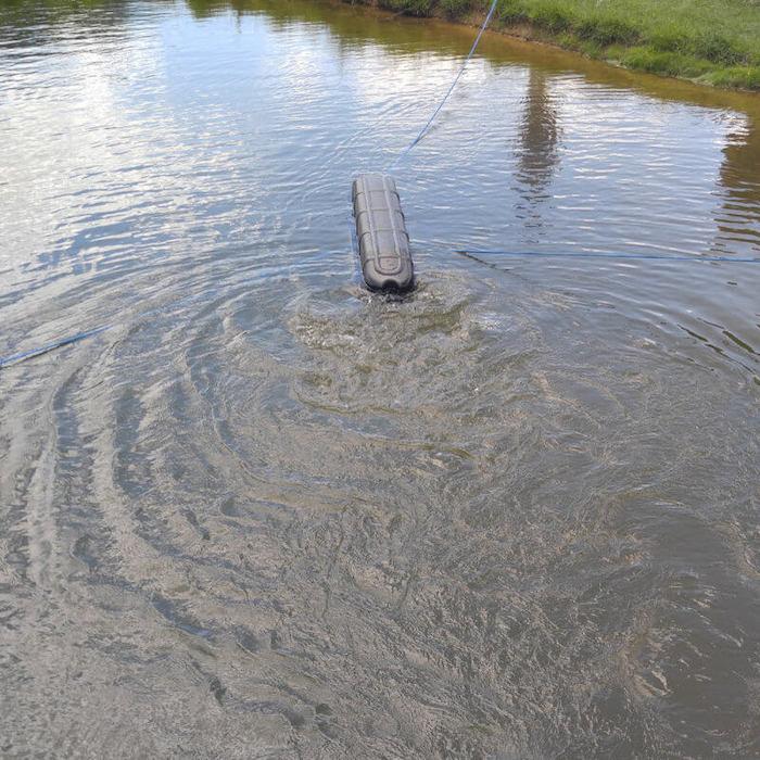 Bearan Aquatics Flo-Gen Aerator floats in a pond. The black float is the only portion of the Flo-Gen visible. You can see that it is attached to land by a blue mooring rope.