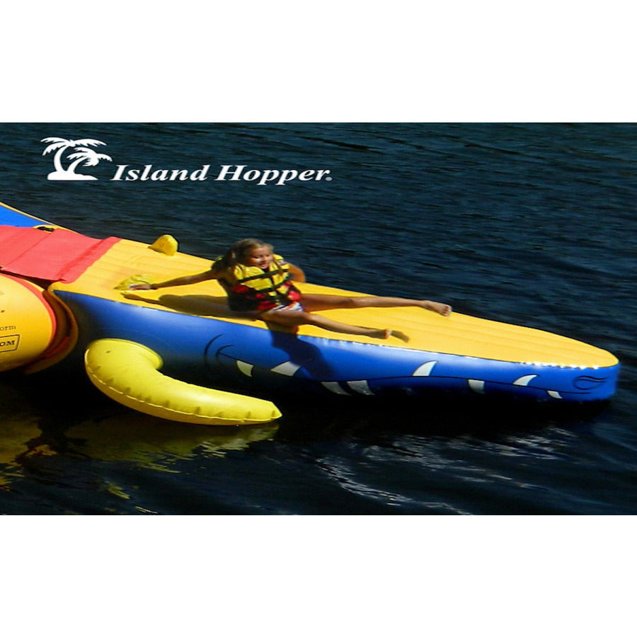 A young boy sliding down the tail attachment slide of the Island Hopper 15' Gator Monster Water Trampoline Water Park