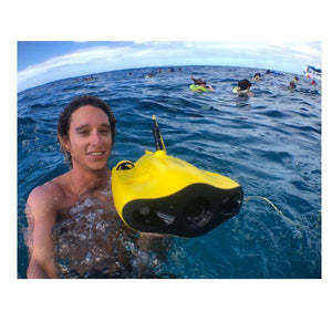 Young man holds a Chasing Gladius Mini Underwater Drone just above the surface of the water.  The yellow underwater drone for sale pops against the blue ski and dark blue water.