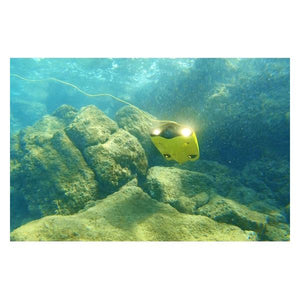 Underwater view of the Chasing Gladius Mini Underwater Drone with its LED Lights on and facing upward at a 45 degree angle.  The yellow Gladius Underwater Drone is near a light brown reef and the water is clear.