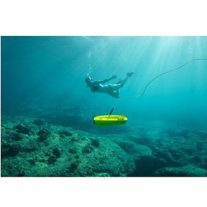 Chasing Gladius Mini Underwater Drone explores near the ocean floor while a scuba diver is nearby in the background.  The water is blue and clear and the yellow Gladius Under Water Drone is clearly visible.