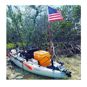 View of a kayak on the beach with an orange cooler and American flag upright 5 feet tall.  Bixpy Hobie Twist & Stow Kayak Rudder Adapter is attached and folded onto the back of the kayak.