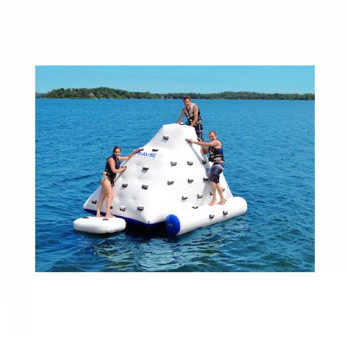3 young adults climbing on a white Rave Floating Inflatable Iceberg 7 on a lake against a blue sky. 