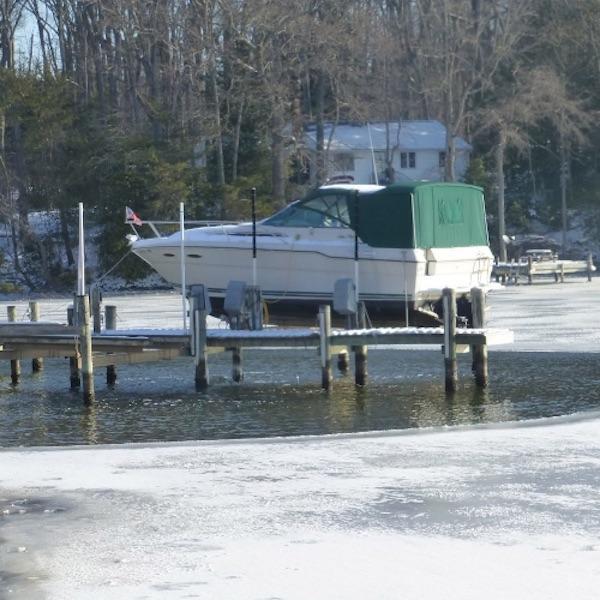 This image shows a docked boat on a life on a frozen lake.  There is Kasco De Icer in place that has opened up a large circular hole in the ice.
