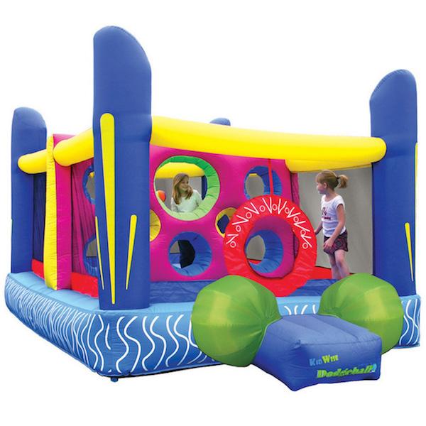 KidWise Jump&#39;n Dodgeball Sports Bounce House display image on white background.  Blue base with 4 big blue inflated support post in each corner.  Yellow cross bar connects the supports.  Green balls adorn the side of the entry ramp.  You can also see the middle partition with round spaces for throwing and climbing, it is violet.  Kids are also playing inside.