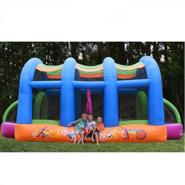 KidWise Arc Arena II Inflatable Sports Bounce House display image. The outside of the lower perimeter is orange and there are 4 inflatable blue supports that go over the top.  Soccer goal is visible with pink outer edge and lime green supports.