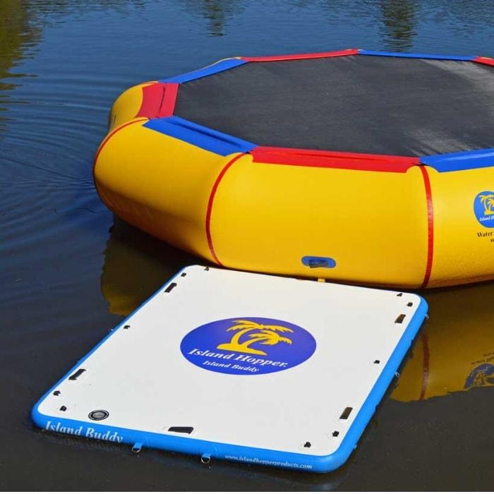 An Island Hopper Island Buddy Inflatable Floating swim platform sits connected to an Island Hopper water trampoline on a lake.  The white and blue Island Buddy inflatable floating dock rests easy on the glass-like dark blue water.