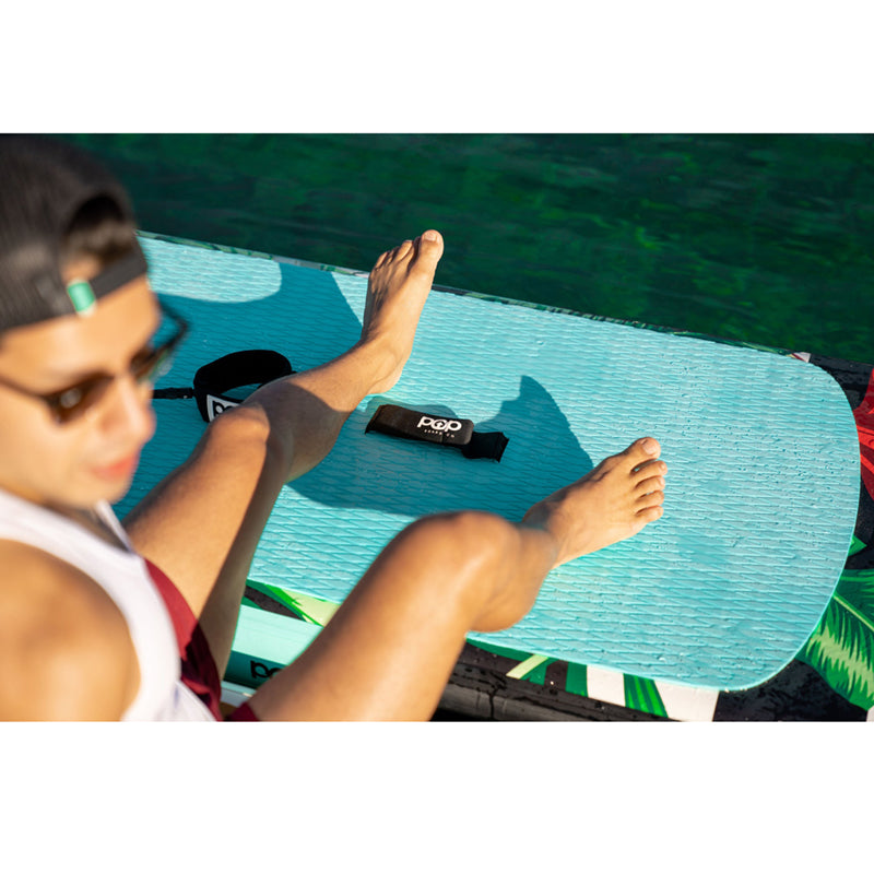 Royal Hawaiian SUP Mint-Black on the water with a person resting their legs on the paddleboard.