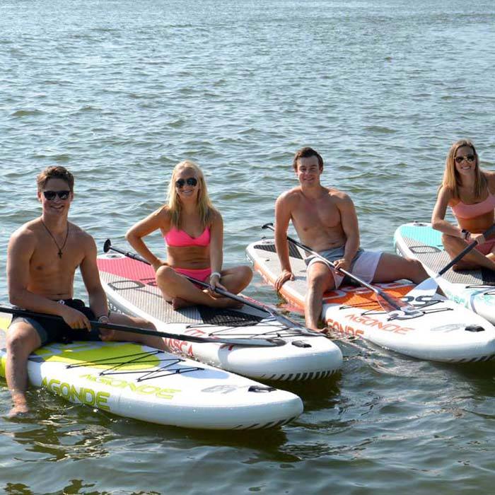 Rave Agonde Inflatable Paddleboards with four different colors and one person sitting on each paddleboard on the lake.