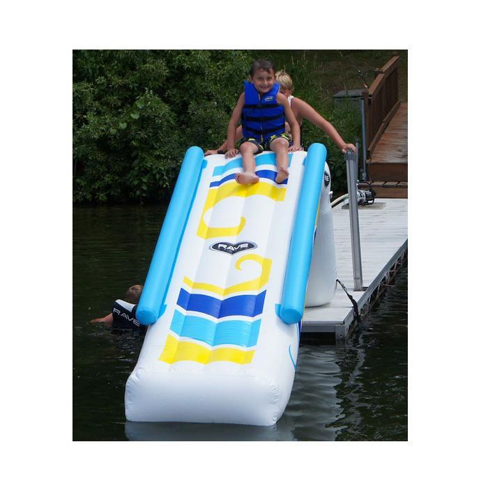 Front view of the Rave Inflatable Dock Slide.  The inflatable dock slide is white with yellow, light blue, and blue highlights on the slide.  There are inflatable light blue railings on either side. A boy is ready to slide down the inflatable water slide.
