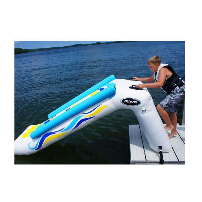 A boy prepares to walk up the climbing stairs on the back of the Rave Inflatable Dock Slide.  This is a side view and you can see the yellow and blue highlights and light blue railings on the inflatable water slide.