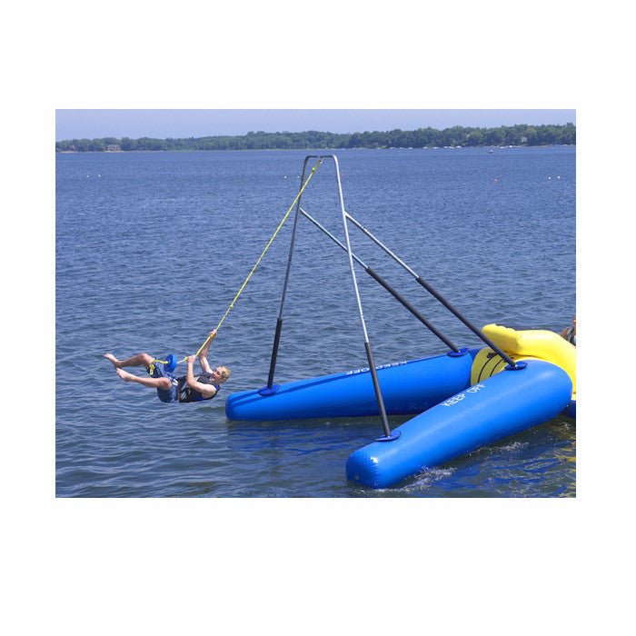 Man swinging on the Rave Rope Swing Water Trampoline Attachment in the middle of the lake.  Rave Rope Swing features blue inner tubes with yellow highlights and an aluminum swing frame with black padding on the bottom portions of the frame. 