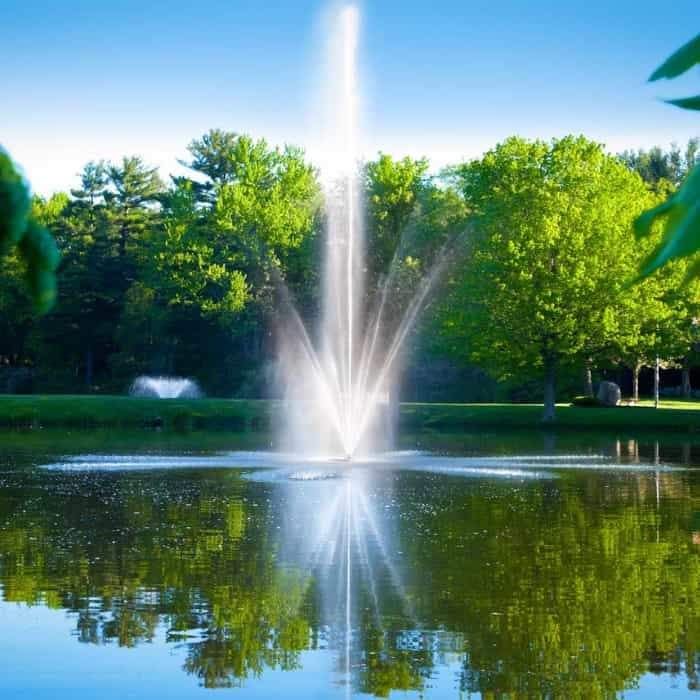 Scott Aerator Atriarch Pond Fountain sits in the middle of pond creating a beautiful spray of water up in the air against green trees in the background.  The Scott Aerator Floating Pond Fountain elegance is on display. This floating fountain is a spectacular sight to see.