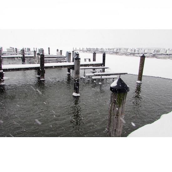 A marina is shown with a deicer in the water.  The water is not frozen in the wooden dock slips but is frozen away from the dock.