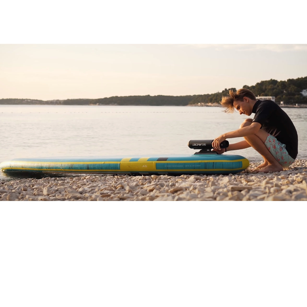 A young adult man attaches a ScubaJet Pro as a paddleboard motor using the overwater kit.