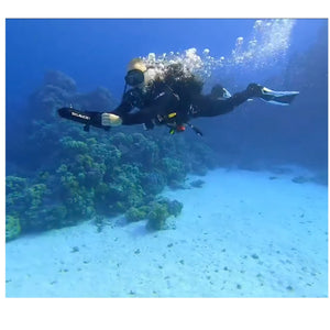 A diver used the ScubaJet Pro Underwater Kit to power the underwater scooter through the water. Air bubbles come out of the divers mouth and air tank.