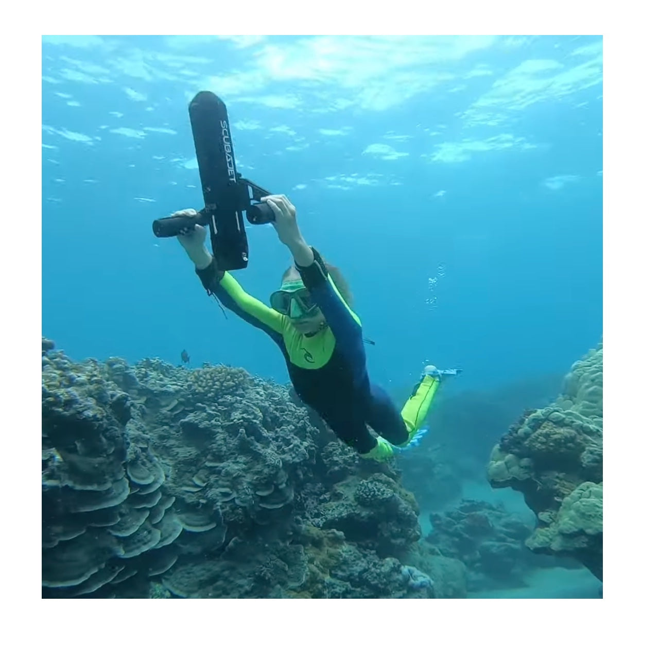 A young girl uses the ScubaJet Pro Underwater Scooter Kit while snorkeling. The ScubaJet Pro is pointed to the waters surface as she heads back up.