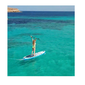 A woman uses the ScubaJet Pro Underwater Kit as a paddle board motor. She holds the paddle above her head as the sup motor powers her out to sea.