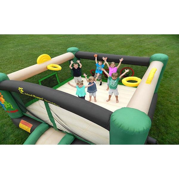 Top view of kids playing in the Island Hopper Sports and Hops 5 Bounce House showing the tan bounce floor, tan slide, yellow basketball hoop, black inflatable support beams, and green support towers.