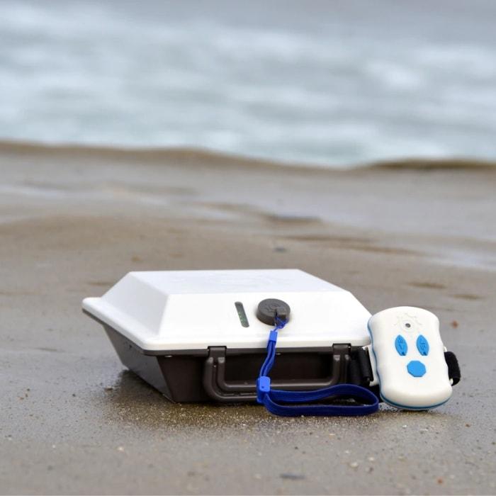 Bixpy Outboard Power Pack with remote shown on a beach next to the ocean.