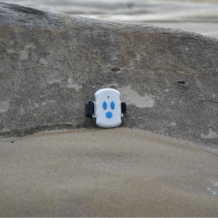 Bixpy Extra Remote for Outboard Power Pack is pictured up against a rock corner.  The remote is white with blue buttons and a black band.