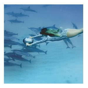 A woman is swimming with an under water scooter. The Yamaha Jet Pod Pro Sea Scooter is being used over a group of dolphins.