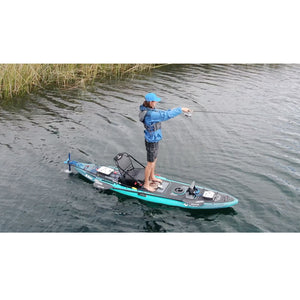 Bixpy Universal Power Pole Kayak Adapter  is shown in place on a kayak on the beach.  The motor is fully unhinged and in the water while the kayak is on standby with a person standing on it fishing.